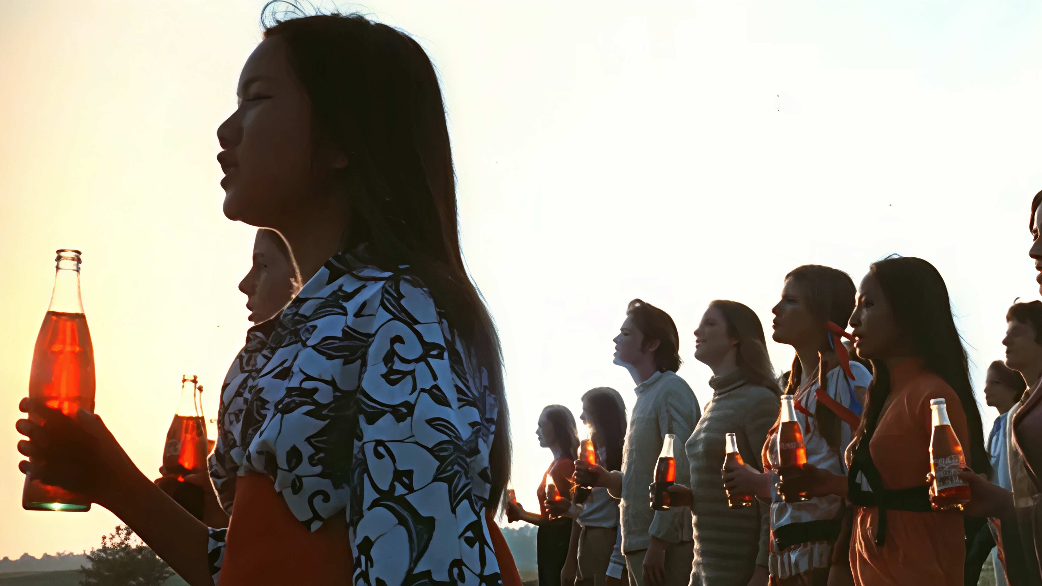 A group of people looking at a fixed point, holding a glass Coca-Cola bottle.