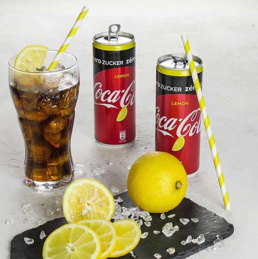 Photo of two cans of Coke Zero Sugar Lemon, with fresh lemon in front of it.