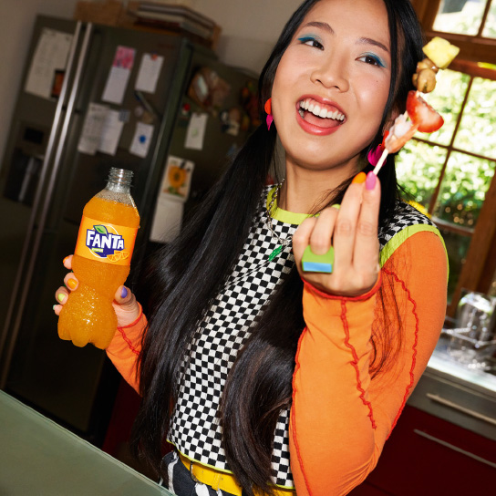Woman with bottle of Fanta and fruit on cocktail stick