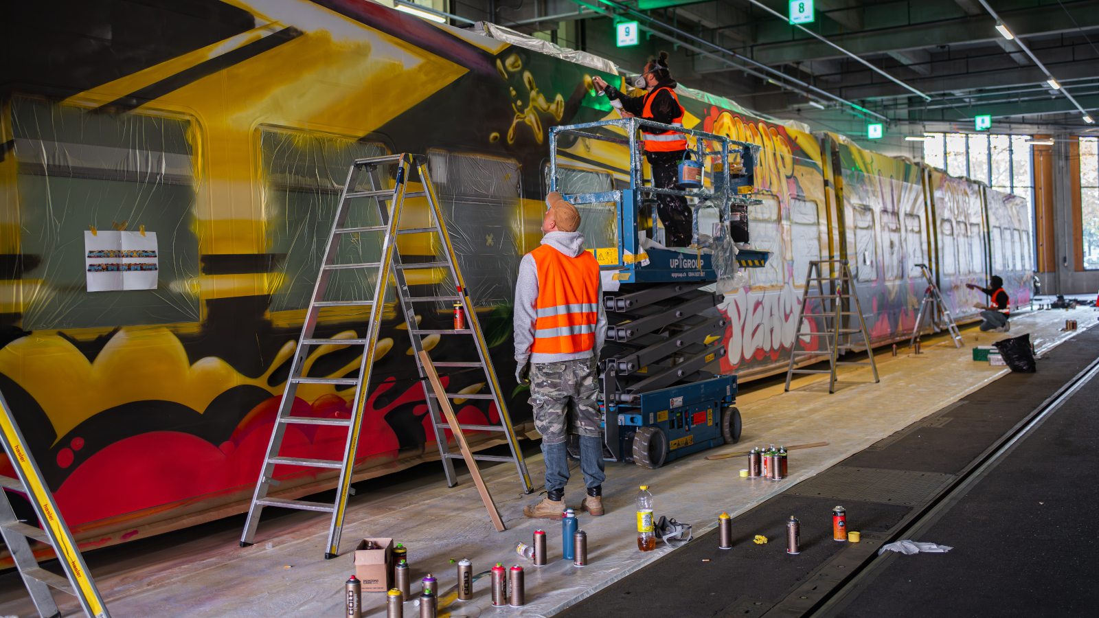 Zwei Künstler besprühen ein Tram in einer Halle