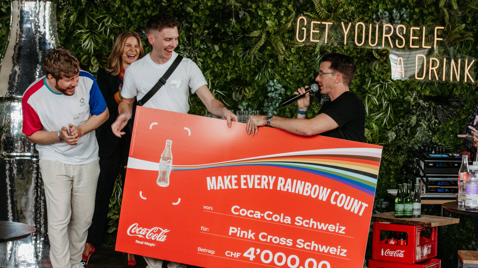 Foto eines grossen Checks im Wert von 4000 Franken, der von Coca-Cola Schweiz and Pink Cross Schweiz übergeben wird