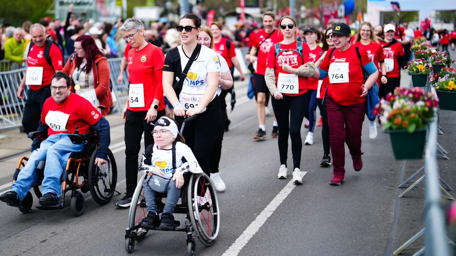 Personen, die im Rollstuhl am Inclusion Run in Wien 2025 teilnehmen mit Läufer:innen im Hintergrund