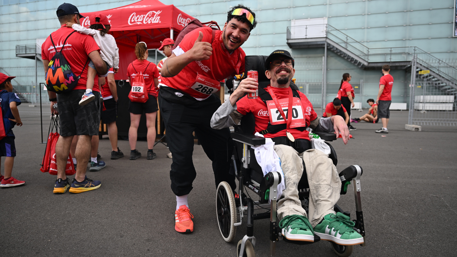 Zwei junge Männer posieren für die Kamera, der Mann im Rollstuhl hält eine Cola