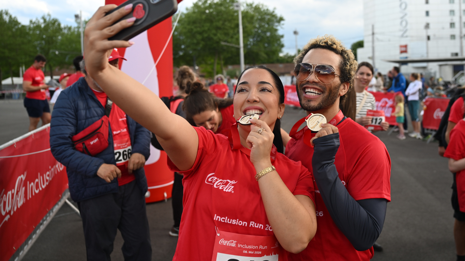 Eine junge Frau und ein junger Mann machen ein Selfie, währenddem sie die junge Frau auf ihre Medaille beisst.