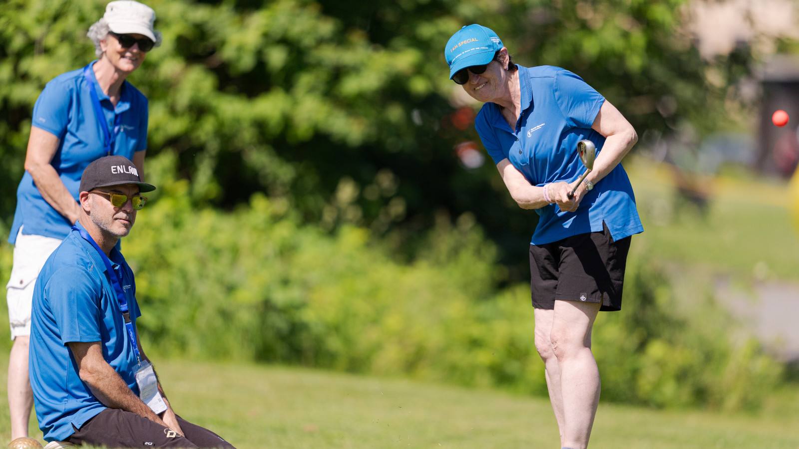 Une athlète effectue un putt sur le parcours de golf, accompagné de deux bénévoles.