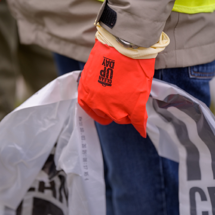 main gantée avec logo Clean up day tenant un sac poubelle