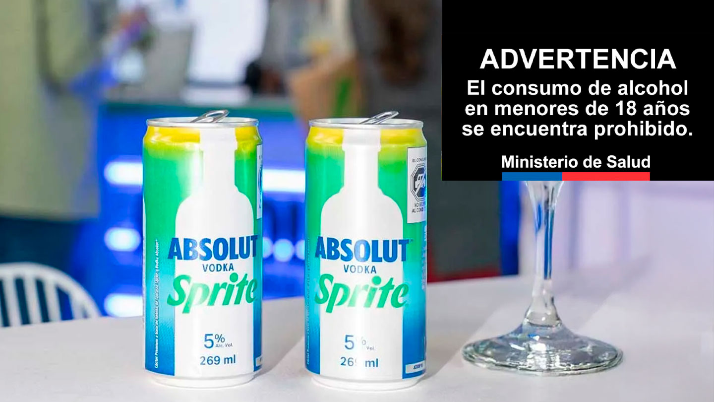 Dos latas de Absolut Sprite y una copa con un elemento verde en una mesa blanca, con un fondo borroso de luces de neón.
