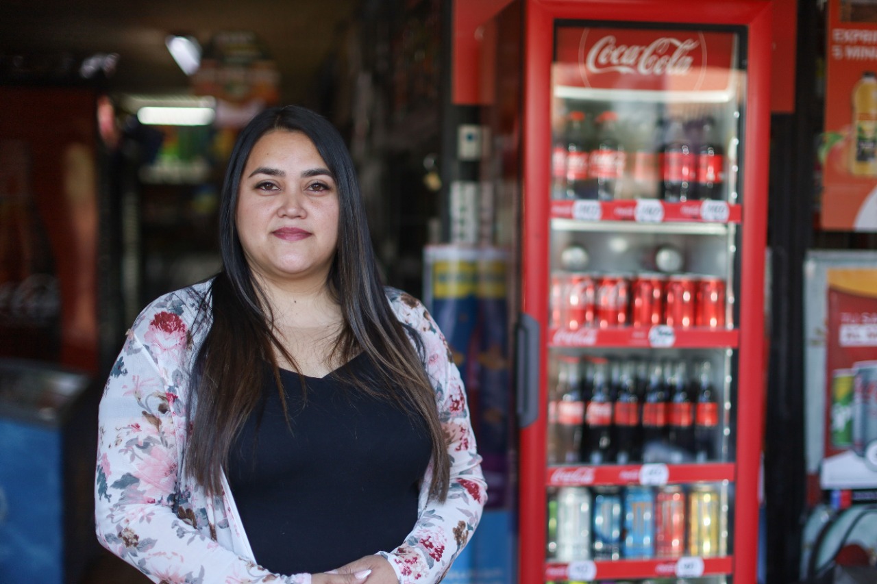 Una mujer parada frente a la tienda minorista y botellas de Coca-Cola en el refrigerador al fondo