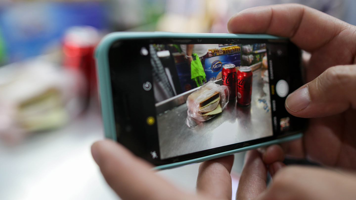 Foto de teléfono celular con imagen de dos latas de Coca Cola y un sandwich