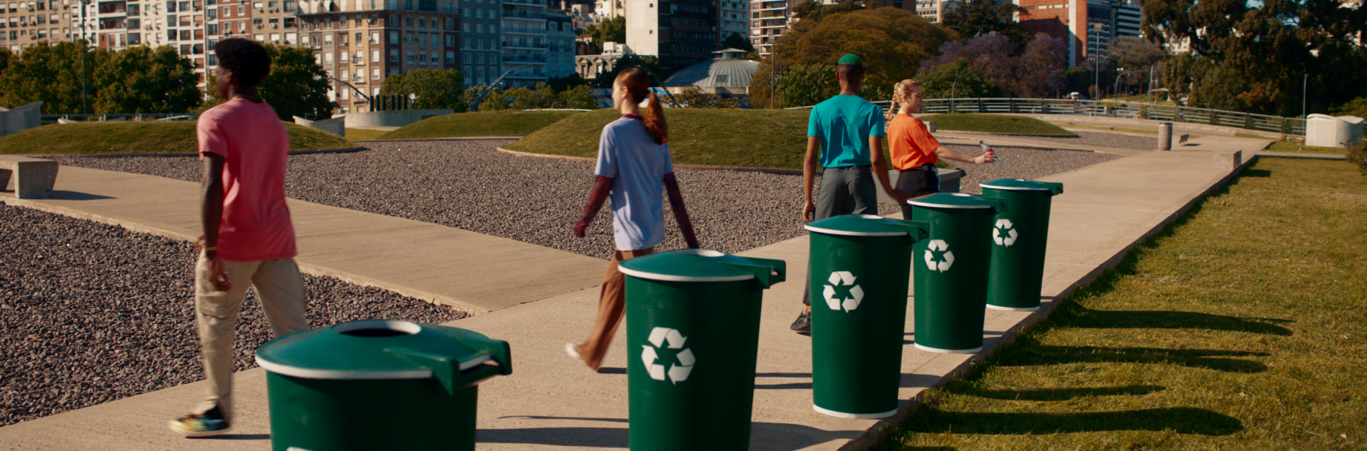 Jóvenes arrojan botellas plásticas en tachos verdes con el logo de reciclaje