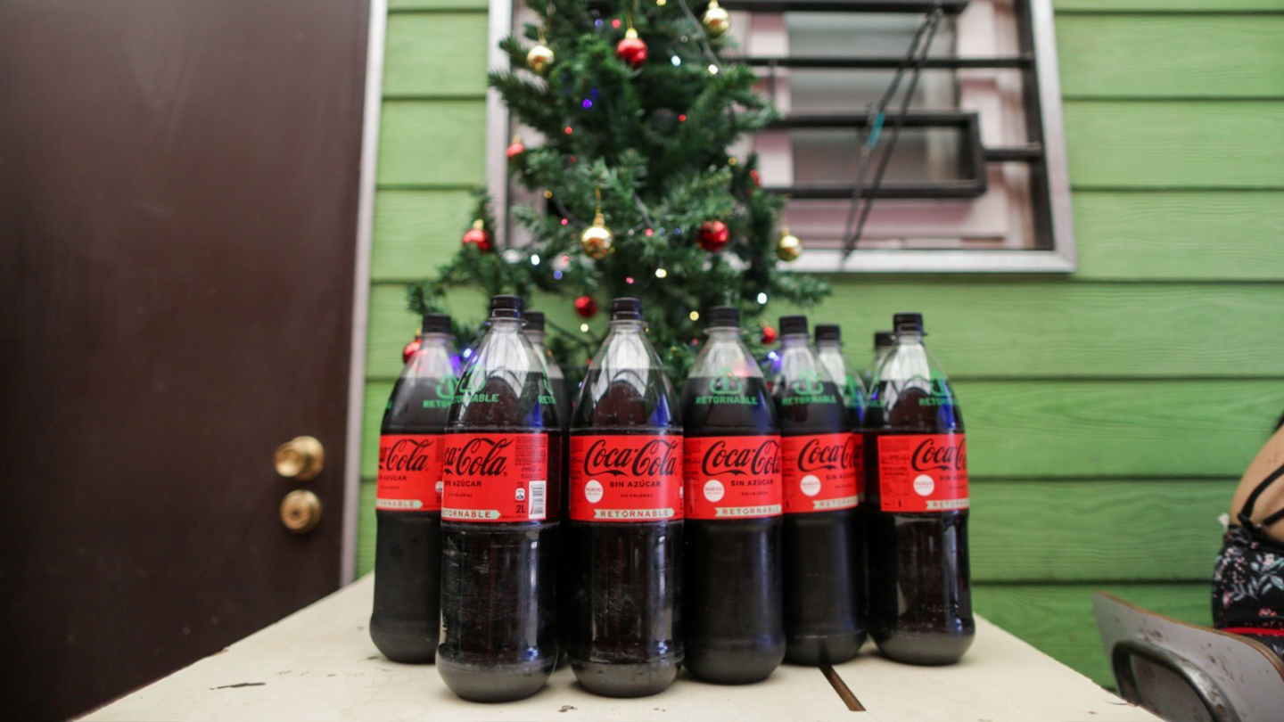 Botellas de Coca-Cola Zero frente a un arbolito de pascua.  Fondo de pared verde con ventana de vidrio y puerta café oscuro.