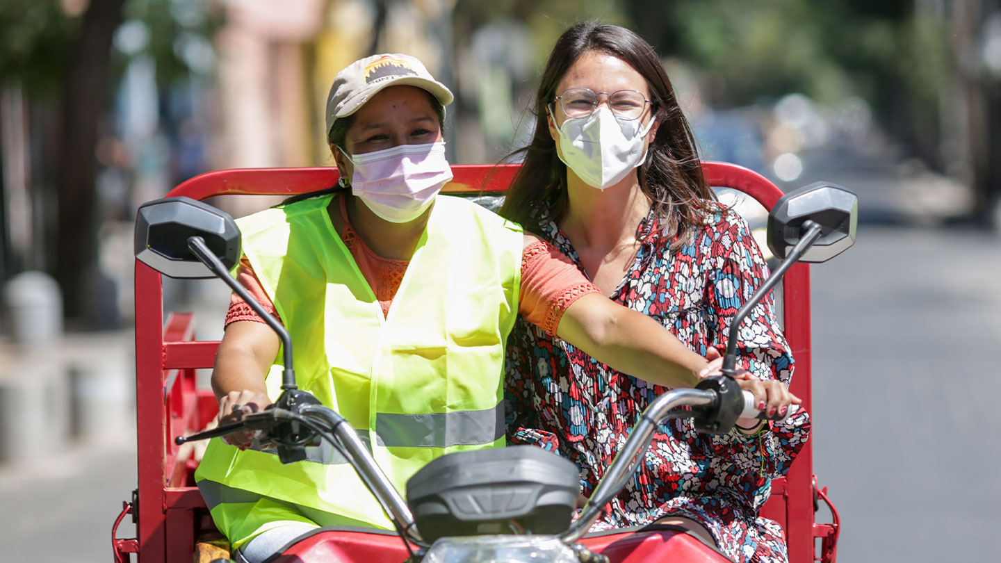 Dos mujeres con mascarilla en un vehículo tipo motoneta.
