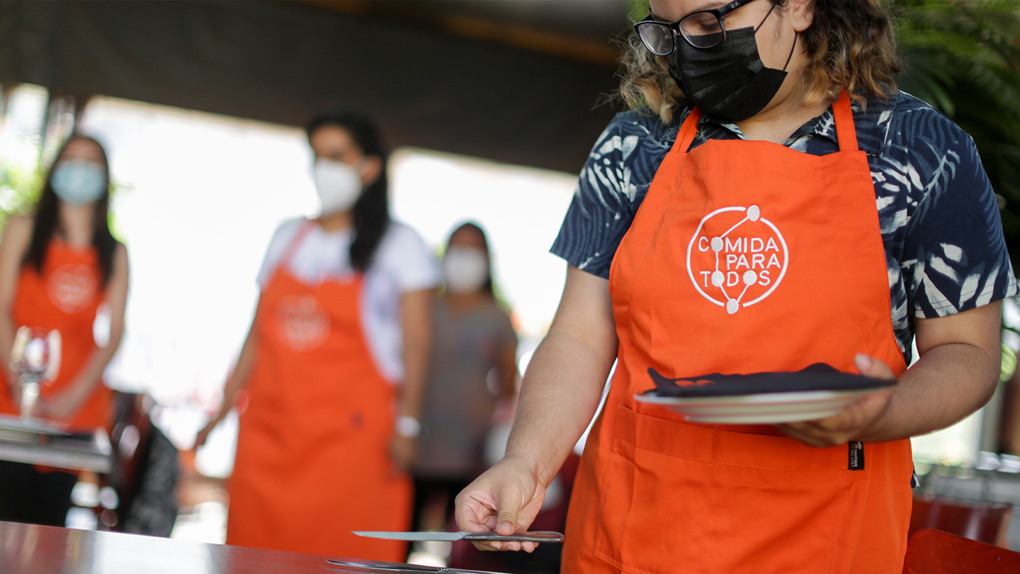 Foto de tres mujeres con delantal naranjo preparando platos.