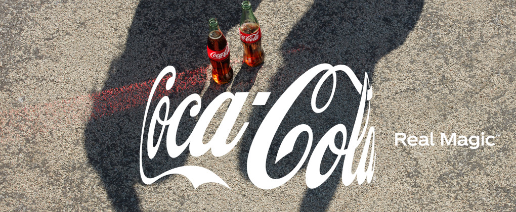 Logo curvado de Coca-Cola sobre dos botellas de Coca-Cola