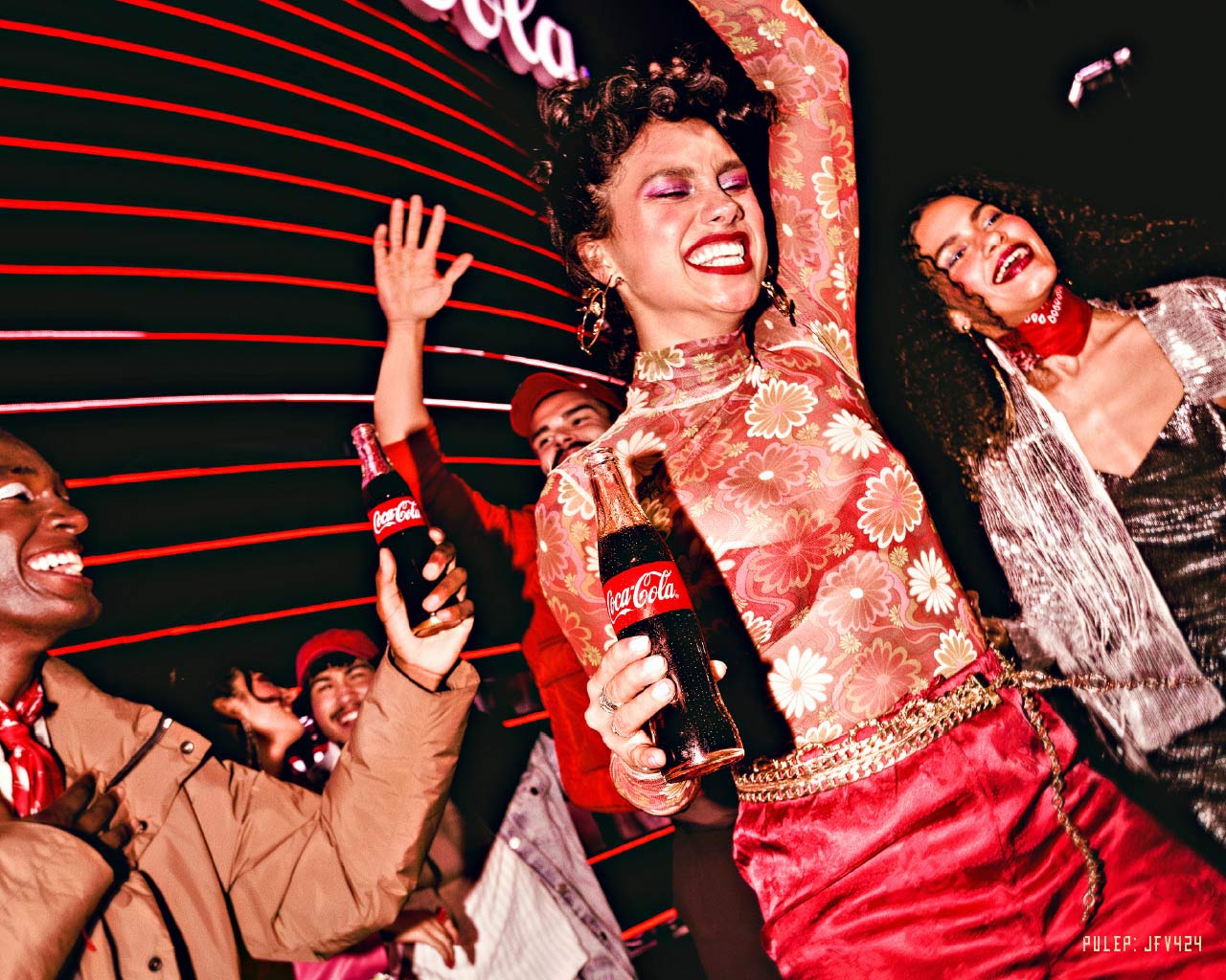  Un grupo de jóvenes diversos y sonrientes disfrutan de una fiesta o concierto, bailando y levantando botellas de Coca-Cola. Las luces rojas horizontales en el fondo crean un ambiente dinámico y festivo.