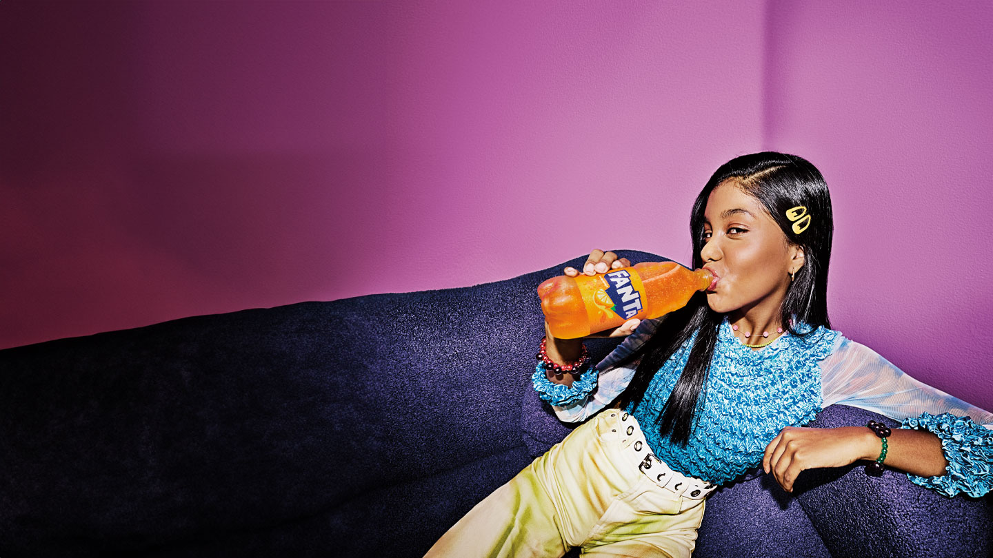 Mujer bebiendo de una botella de Fanta Naranja recostada en un sillon.
