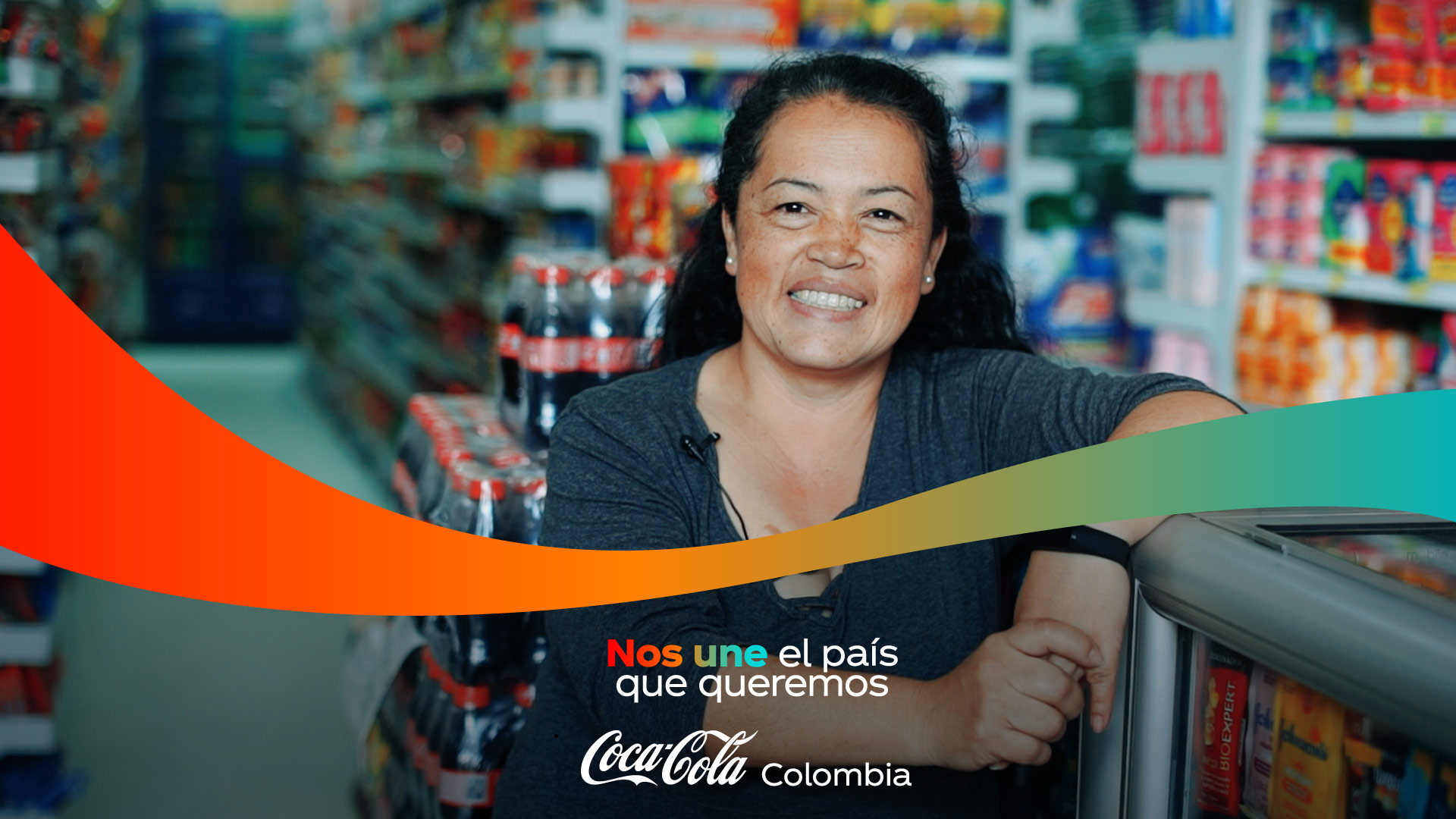 Mujer mirando a cámara sonriente. De fondo se observan productos de Coca-Cola. Se lee la leyenda "Nos une el país que queremos".