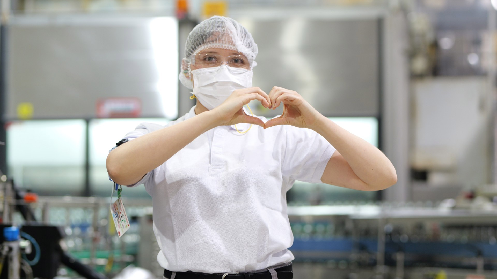 Mujer haciendo un corazon con las manos, tiene puesto un uniforme de trabajo con gorra para el pelo y mascara