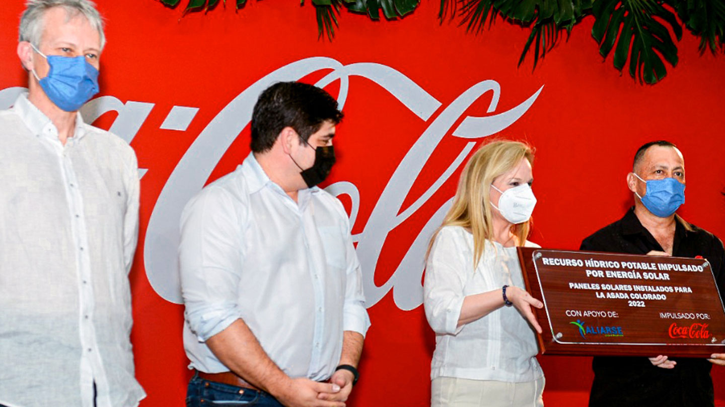 Cuatro personas con un cartel frente a fondo de Coca-Cola