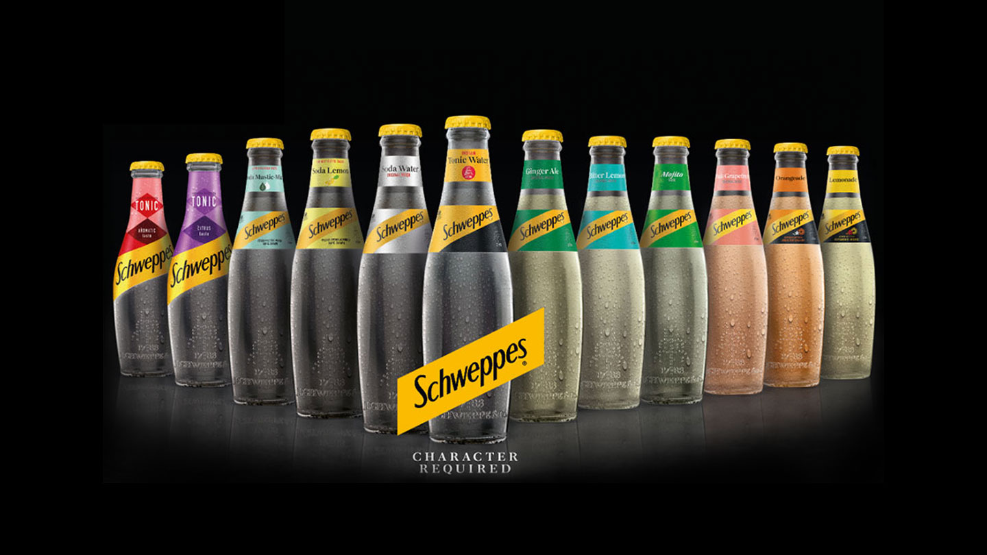 Δώδεκα μπουκάλια με διαφορετικές γεύσεις της Schweppes πίσω από το λογότυπο της Schweppes.