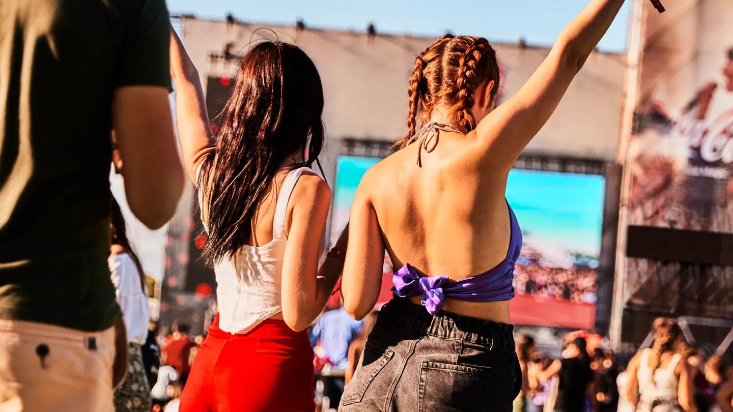 Δύο κοπέλες χορεύουν με τα χέρια υψωμένα μπροστά σε μια μουσική σκηνή σε ένα καλοκαιρινό φεστιβάλ .