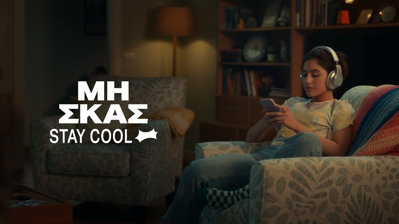 Κοπέλα που κάθεται στον καναπέ κρατώντας κινητό και φορώντας τα ακουστικά της. Λεζάντα: «Μη Σκας Stay Cool»