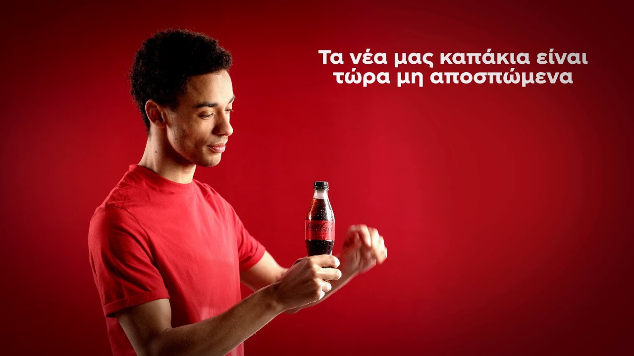 Ένας νέος με μια κόκκινη μπλούζα ανοίγει ένα μπουκάλι Coca-Cola με μη αποσπώμενο καπάκι.