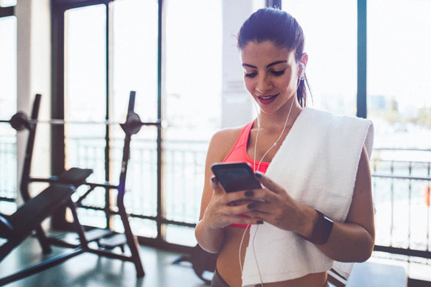 Eine Frau blickt in einem Fitnesscenterauf ihr Smartphone