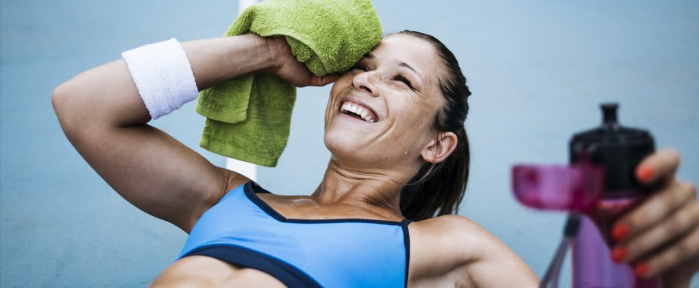 Eine lächelnde Frau nach dem Training, die sich die Stirn mit einem Handtuch abwischt