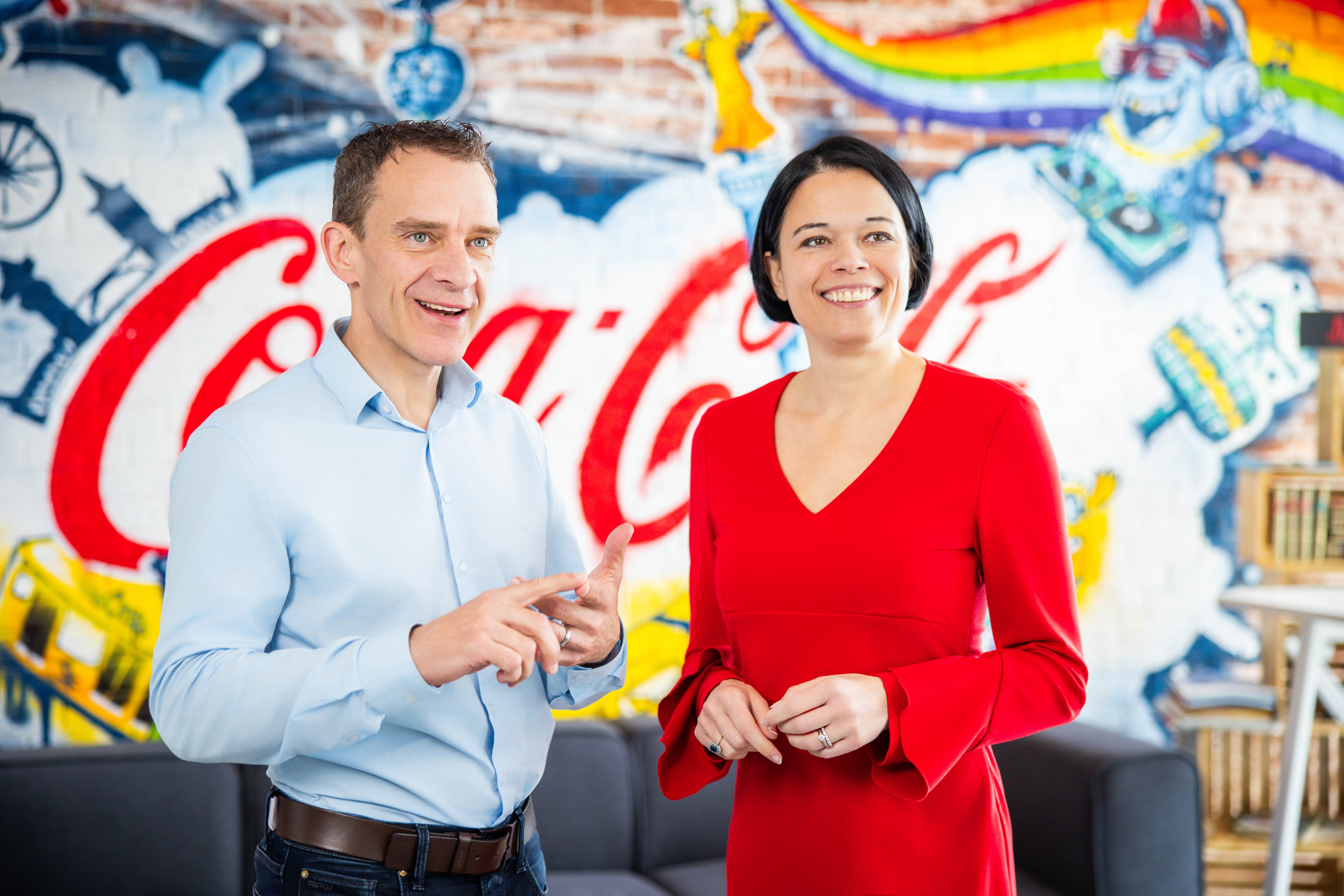 John Galvin und Evelyne De Leersnyder vor einer Wand mit dem Coca Cola Logo