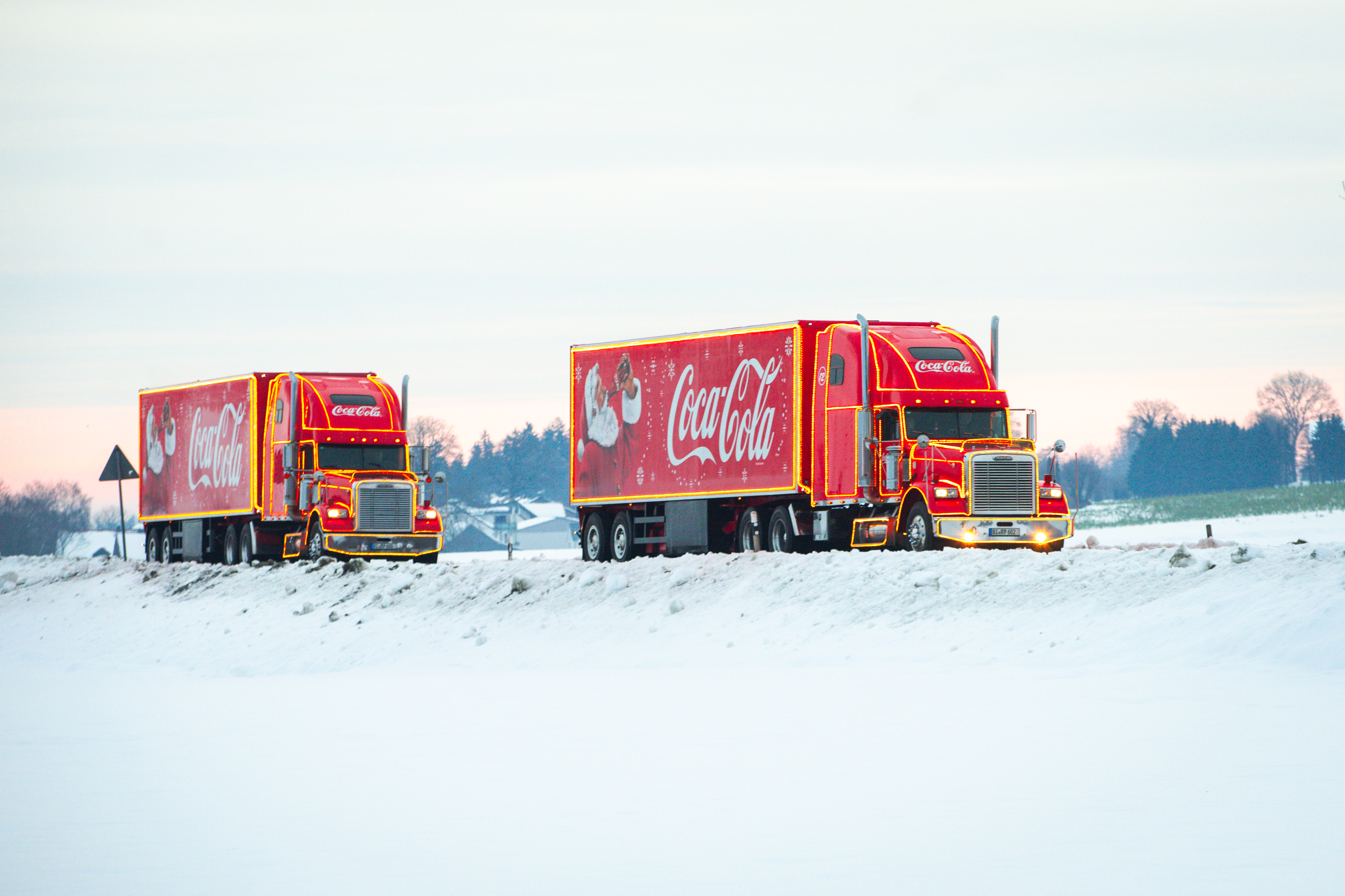 zwei Coca Cola Weihnachtstrucks fahren durch eine schneebedeckte Landschaft