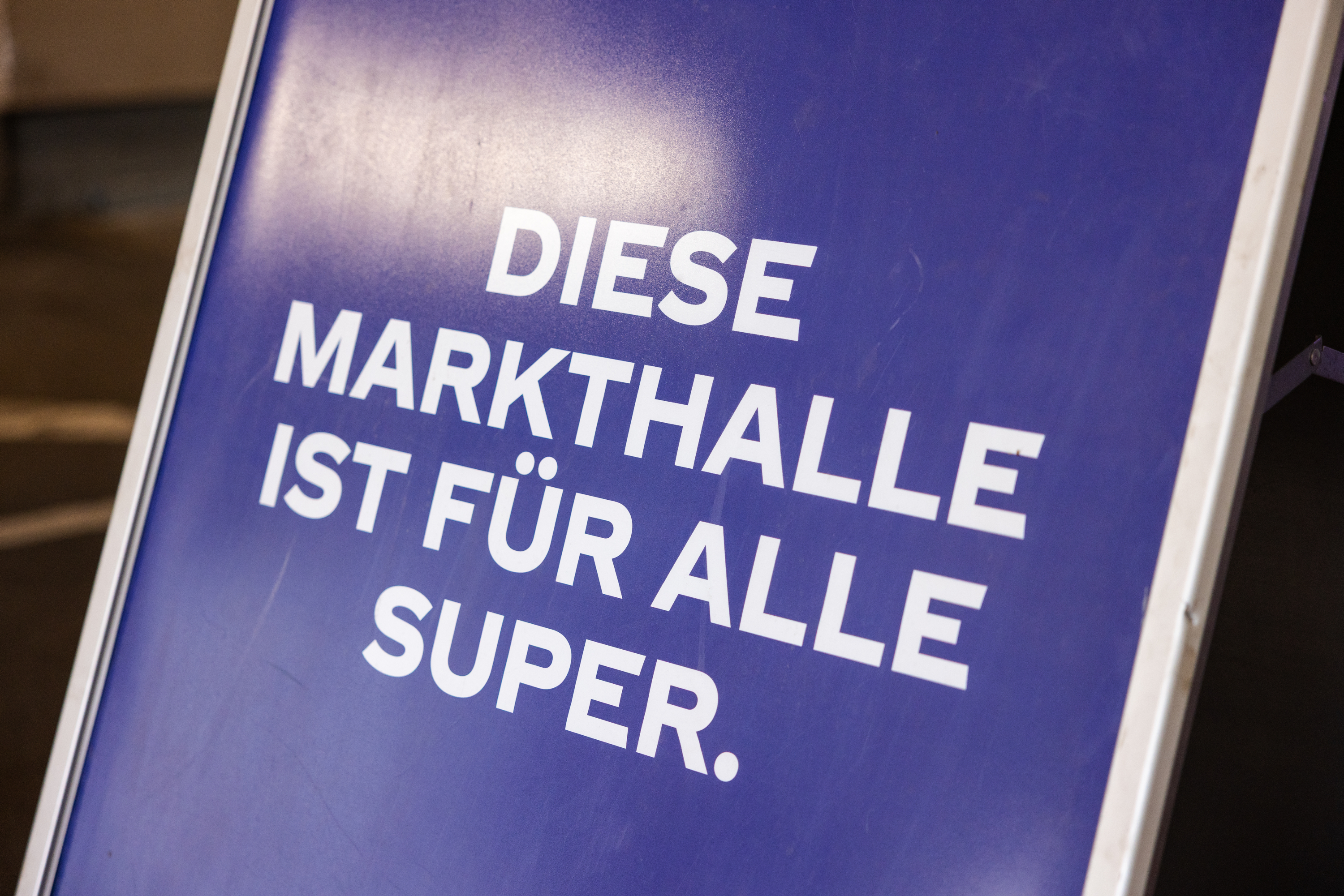 Blaues Schild mit der Aufschrift „Diese Markthalle ist für alle super.“ als Hinweis auf ein inklusiveres und zugänglicheres Einkaufserlebnis.
