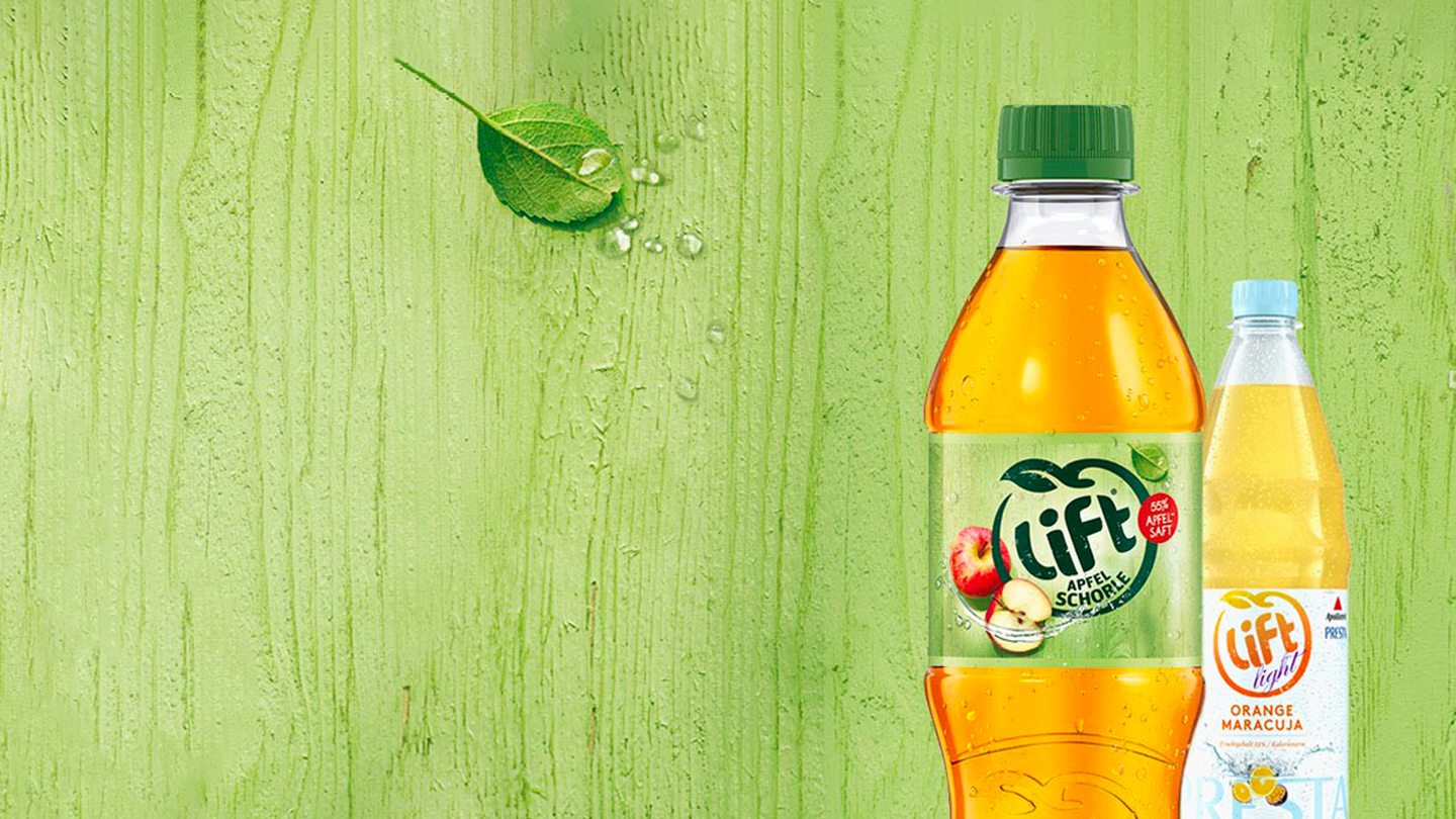 Grüner Hintergrund, davor rechts eine Flasche Lift Apfelschorle und eine Flasche Lift light Orange Maracuja. Links auf dem Hintergrund ein ganzer und ein halbierter Apfel.