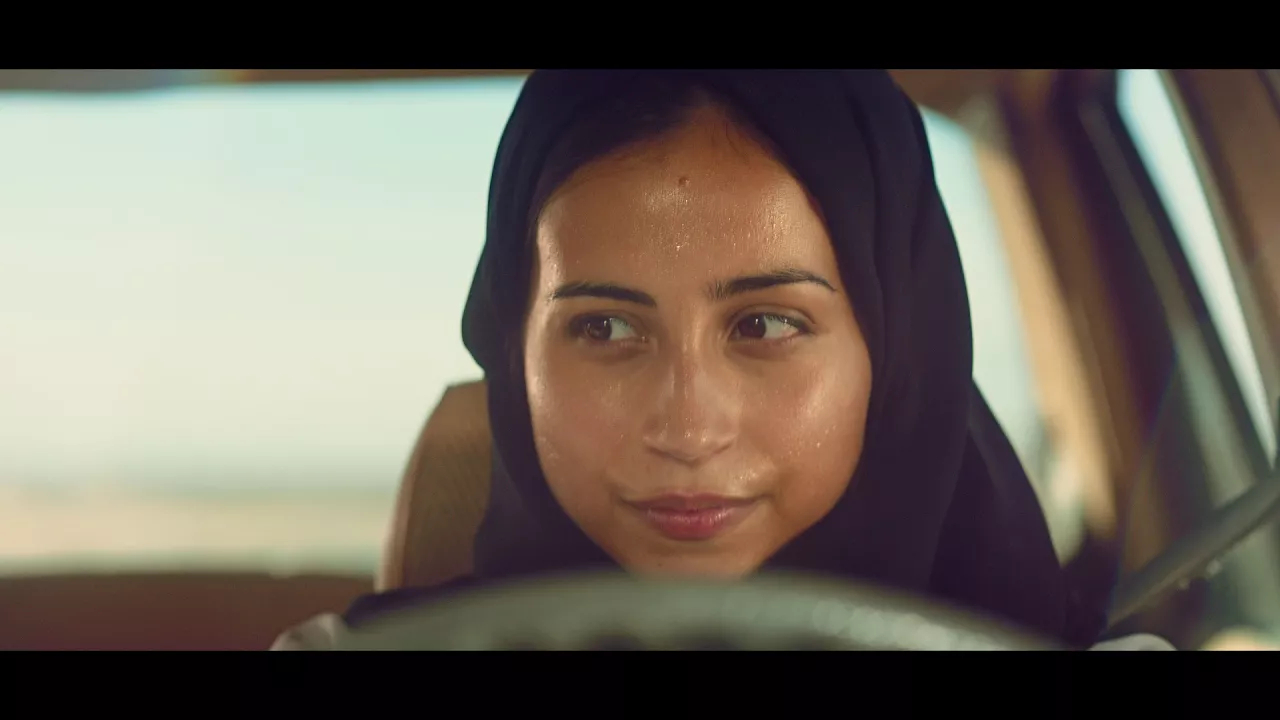 Video-Standbild, auf dem eine Frau hinter dem Steuer eines Autos zu sehen ist.