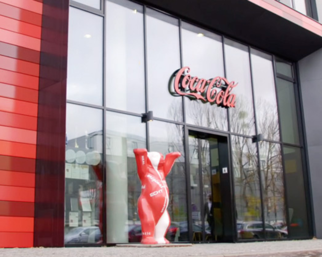 Coca-Cola Mehrweg Flasche vor einem Produktionsstandort