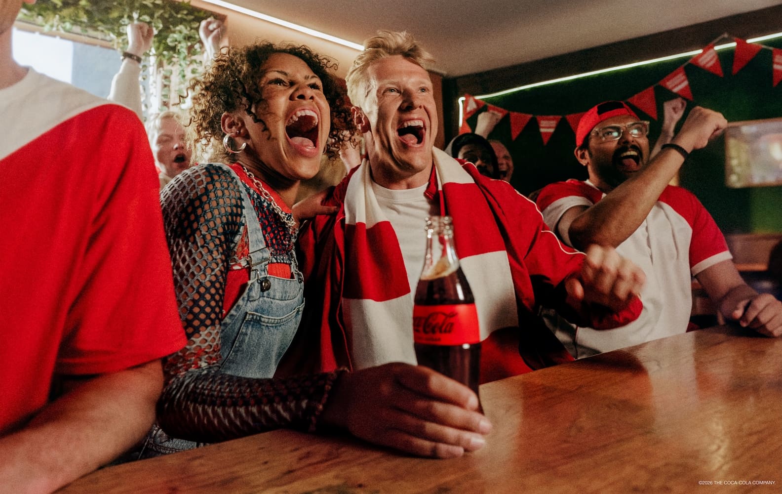 Begeisterte Menschen schauen Sport und trinken Coca-Cola.