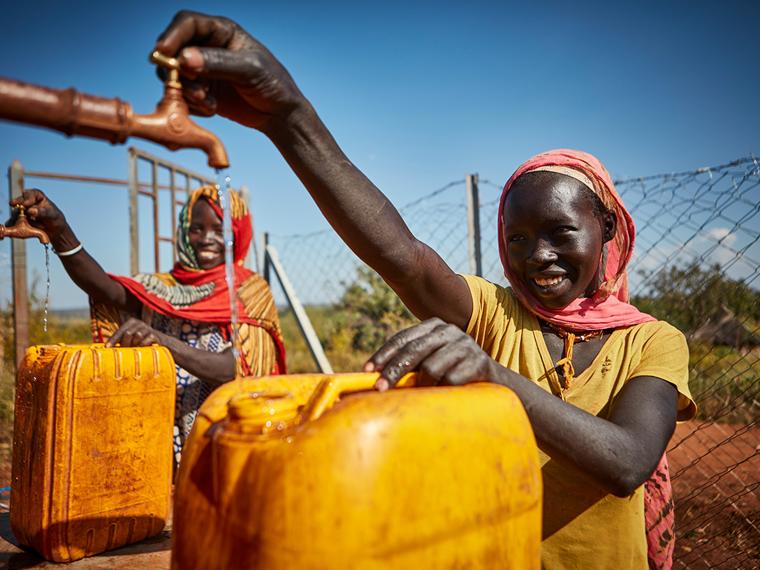 Zwei afrikanische Frauen füllen Wasser in Kanister