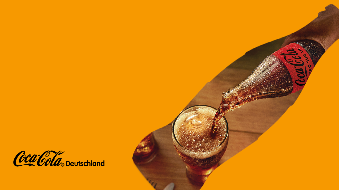 Eine Hand gießt Coca-Cola Zero Sugar aus einer gekühlten Glasflasche in ein Glas mit Eis. Im Vordergrund links steht das Logo von Coca-Cola Deutschland auf orangem Hintergrund.
