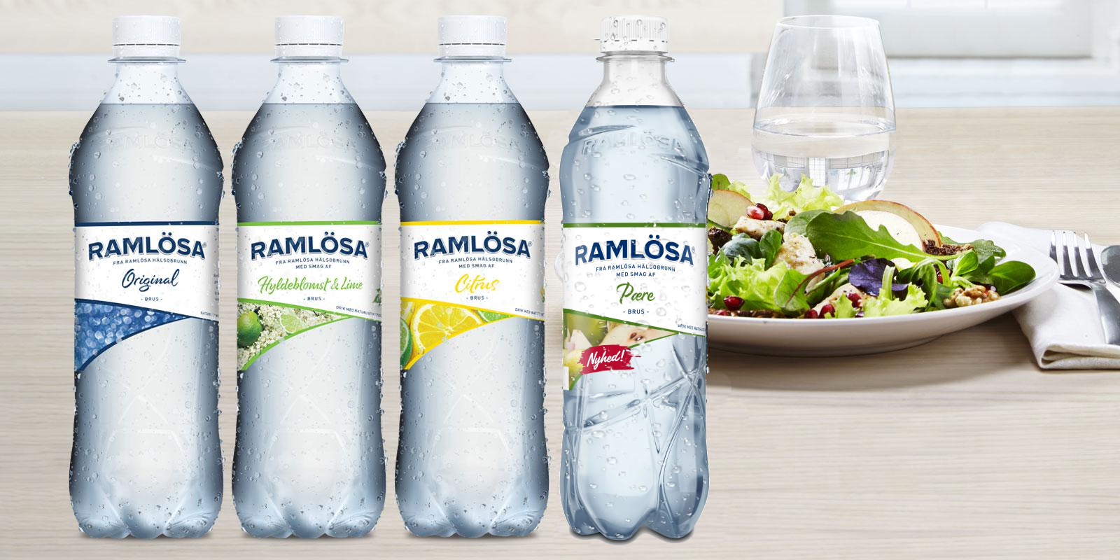 Grafik med fire varianter af Kildevæld-plastikflasker stående på spisebord med salatret, bestik og fyldt vandglas