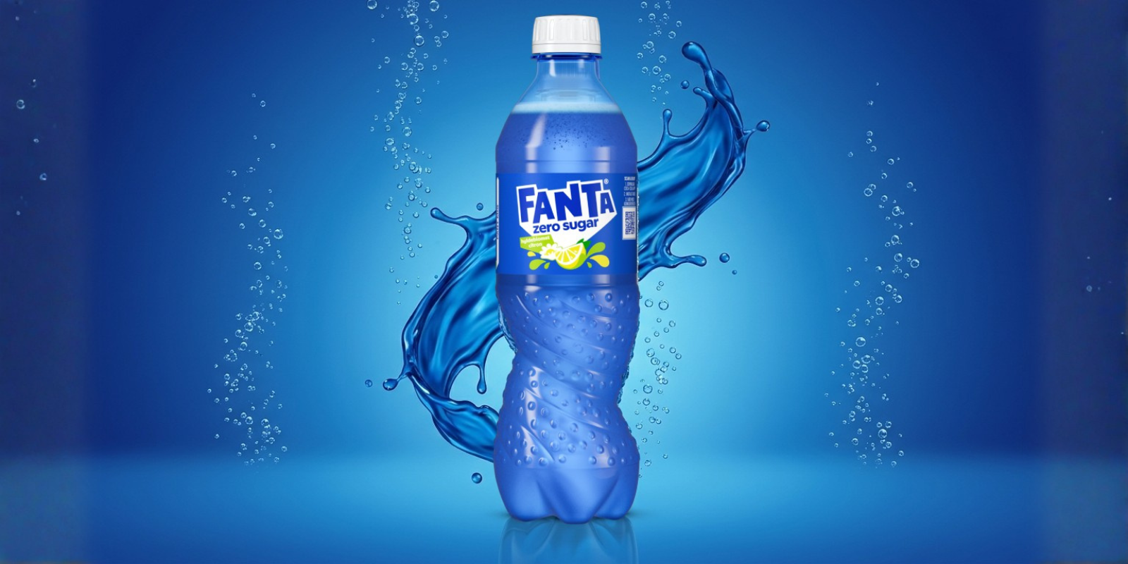 Et blåt plastikflaske med Fanta Zero Sugar står centreret mod en blå baggrund. Flasken er omgivet af et dynamisk vandsplash og små bobler, som giver et friskt og køligt udtryk. Etiketten er tydelig og viser Fanta‑logoet med citron/lime‑grafik.