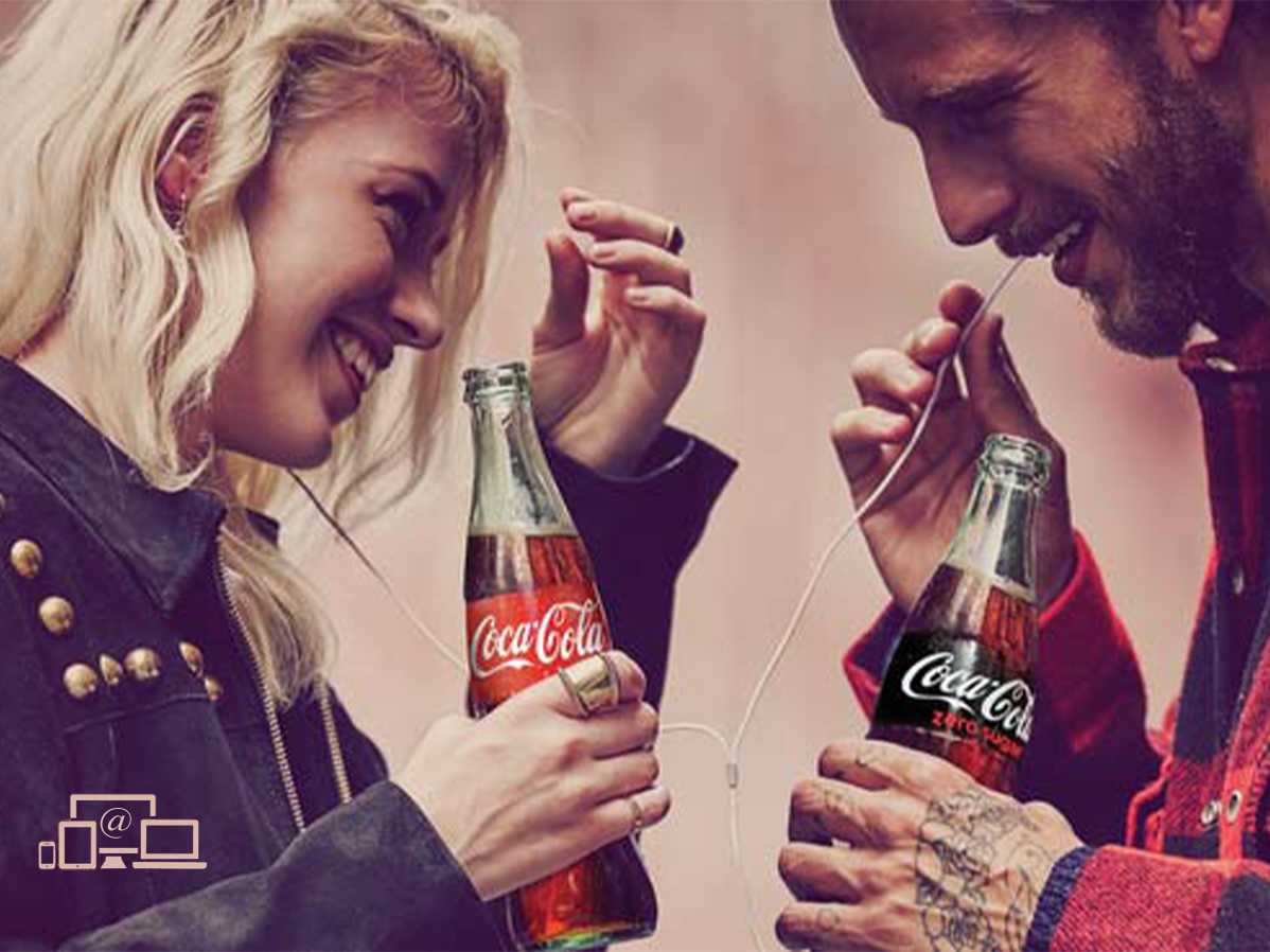 En smilende kvinde og mand står med henholdsvis en Coca-Cola og Coca-Cola Zero, mens de deler et par høretelefoner.