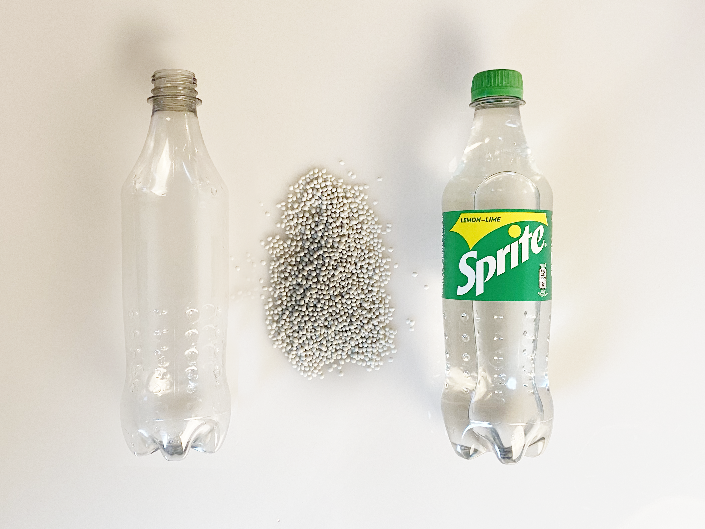 Tom, etiketløs plastikflaske ligger ved siden af små perler samt en klar Sprite-flaske af genanvendt plastik