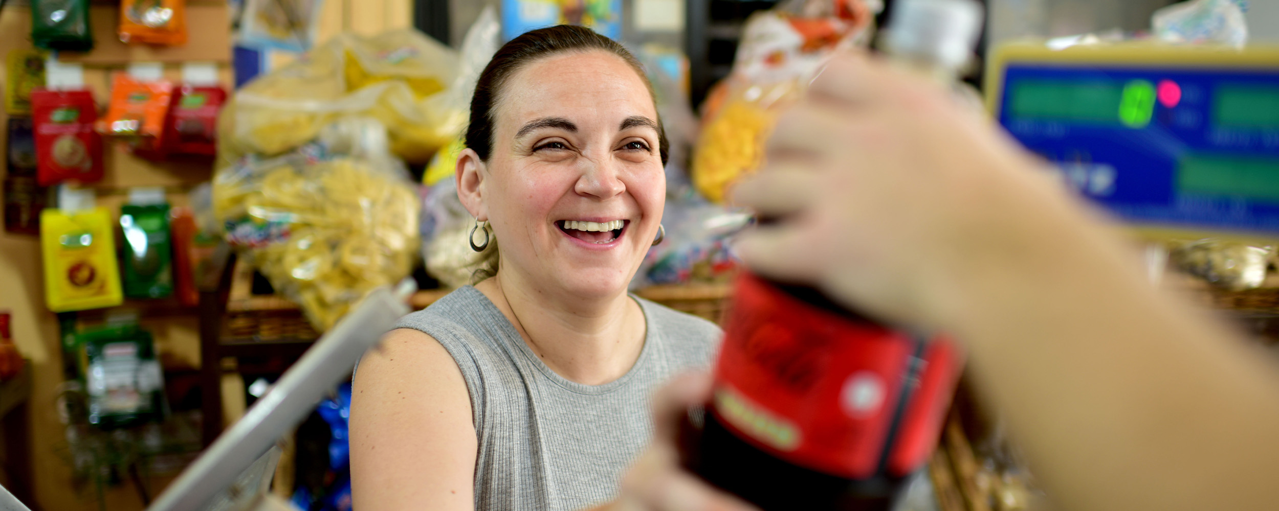 Una mujer sonriente, recibe una botella de Coca-Cola en una tienda