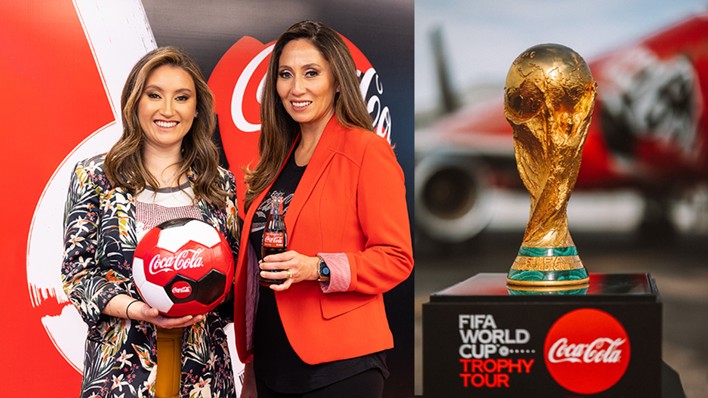 Dos mujeres sujetan un balón de Coca-Cola junto a imagen del trofeo de la FIFA