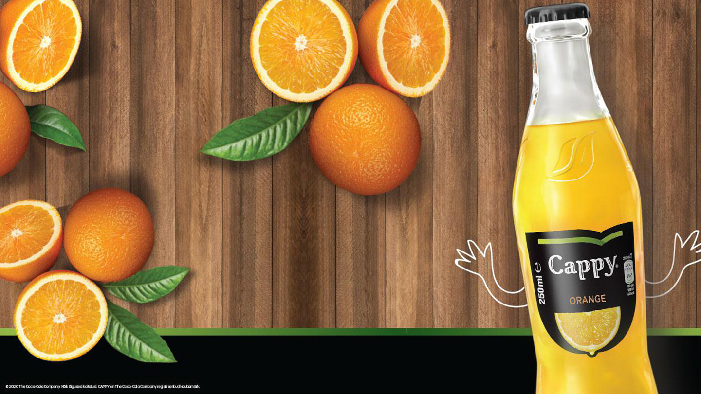  Õnnelik Cappy Orange pudel kätega. Taustal on lõigatud apelsiinid ja laud puidust.