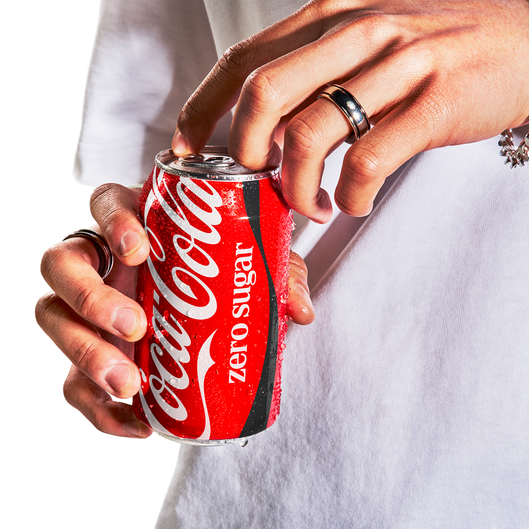 Cilvēks atver sarkanu Coca-Cola bundžu.