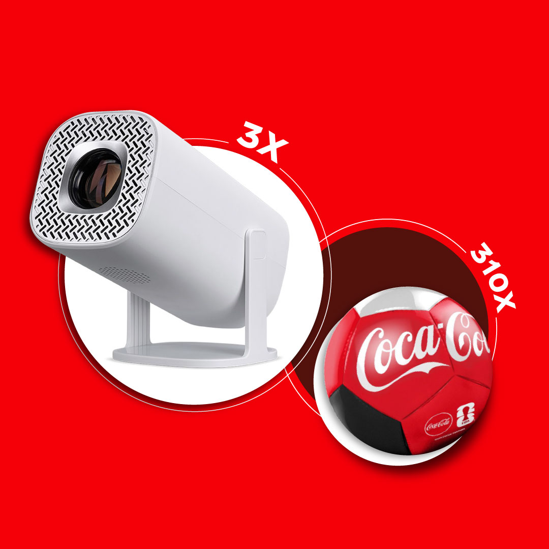 Käes hoitav mini‑projektor ja Coca‑Cola pall punasel taustal, 3× suurendus.