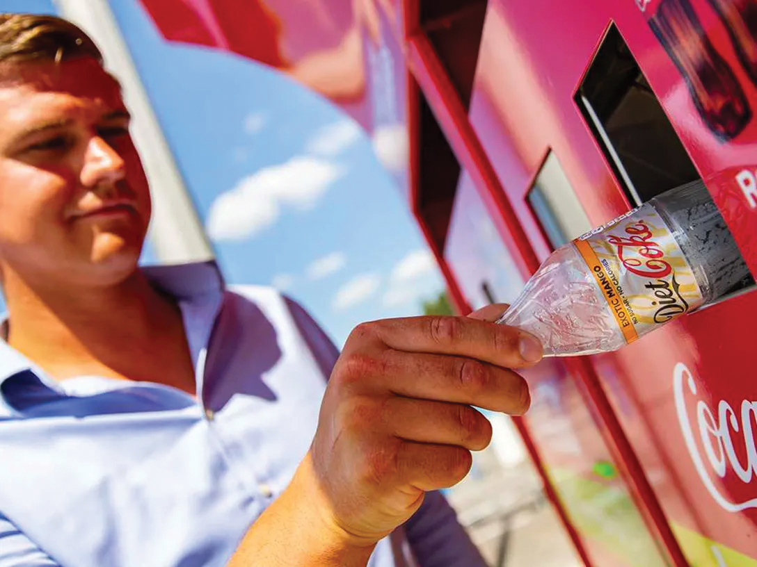 Detail of a hand of a man putting an empty Coca-Cola plastic bottle in a recyclable trash bin