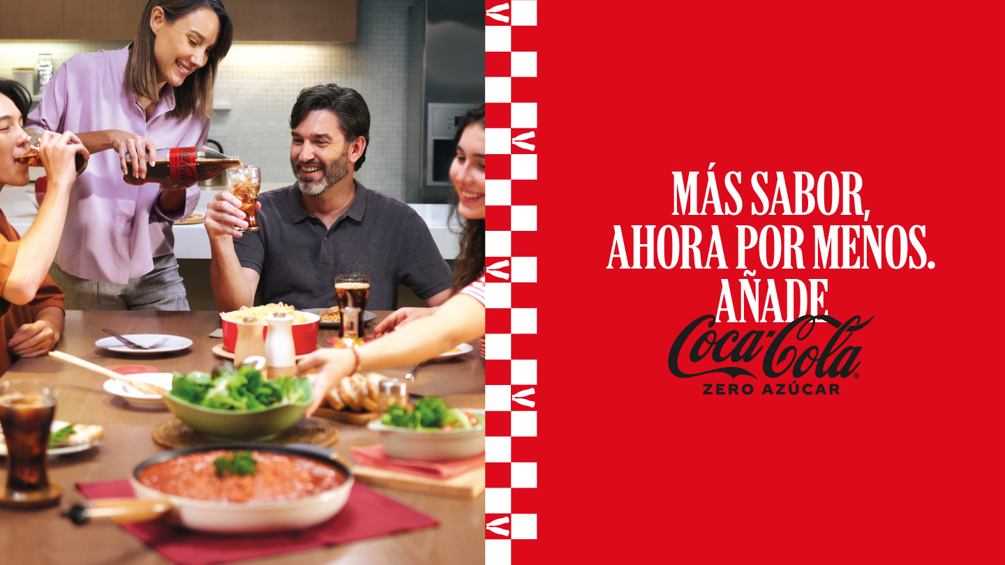 Grupo de personas compartiendo comida y bebidas en una mesa, con vasos de Coca‑Cola, junto a un panel rojo con el texto “Más sabor ahora por menos. Añade Coca‑Cola Zero Azúcar