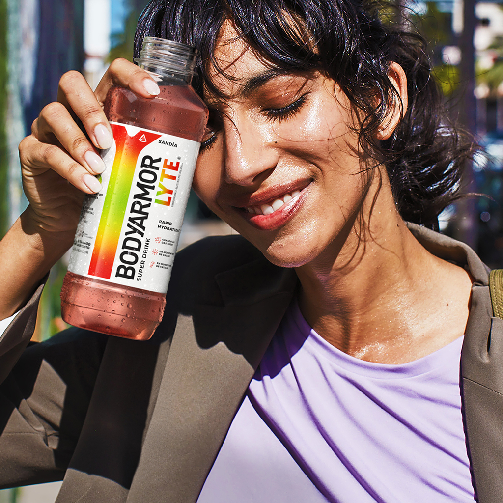 Chica sudando y sonriendo, bebiendo una botella de BodyArmour Lyte sabor Sandía
